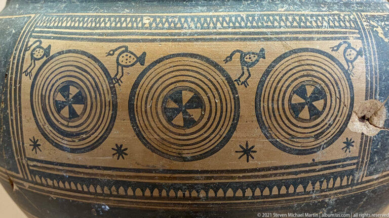Painted ceramic panel with three concentric-circle motifs, central rosettes, small animals, and geometric borders.