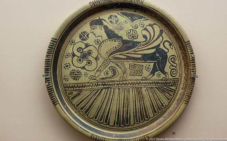 Round painted plate with a large winged fantastic creature, geometric motifs, and radiating border decoration.