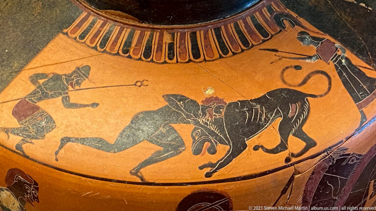 Black-figure vase scene with a human figure confronting a large feline as another figure approaches from the left.