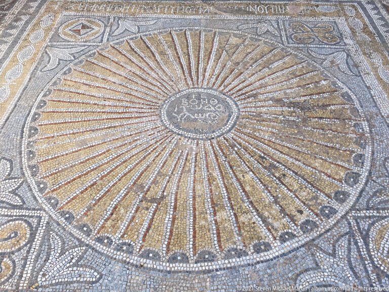 Oblique close view of a golden radial mosaic converging on a Greek-inscribed central roundel with scalloped edging.