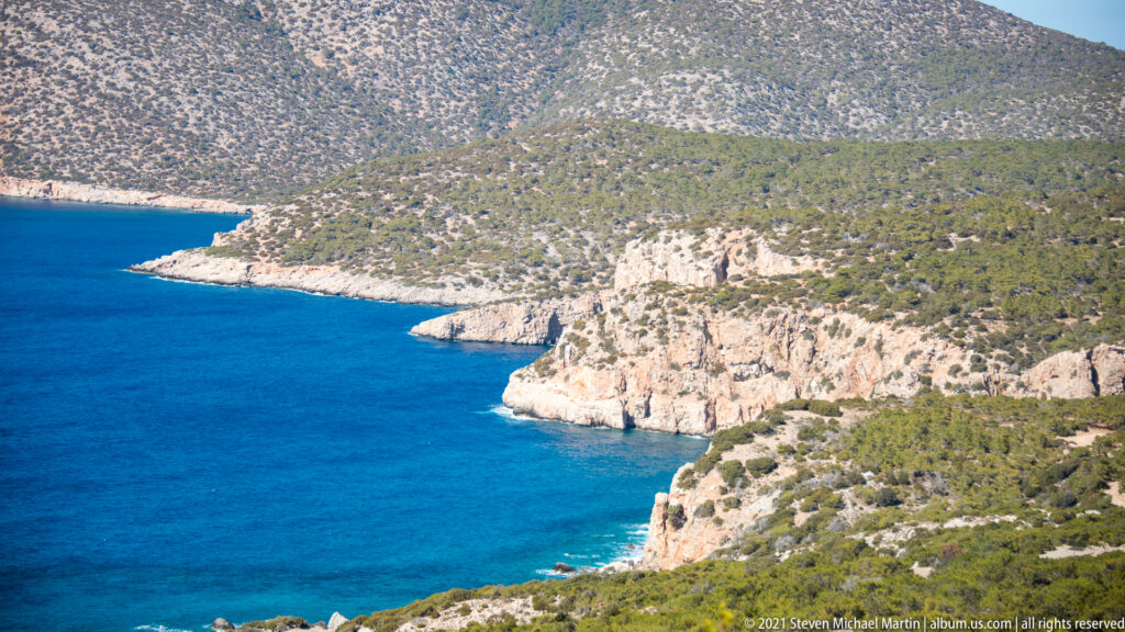 Turquoise coves curve beneath pale limestone cliffs and scrub-covered hills along the Rhodes coastline.