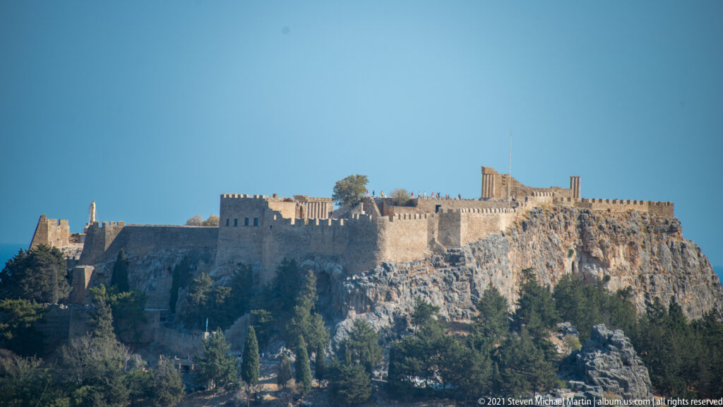 Acropolis of Lindos on a sheer rocky hill, with massive fortification walls, battlements, and ancient columns visible on the summit.