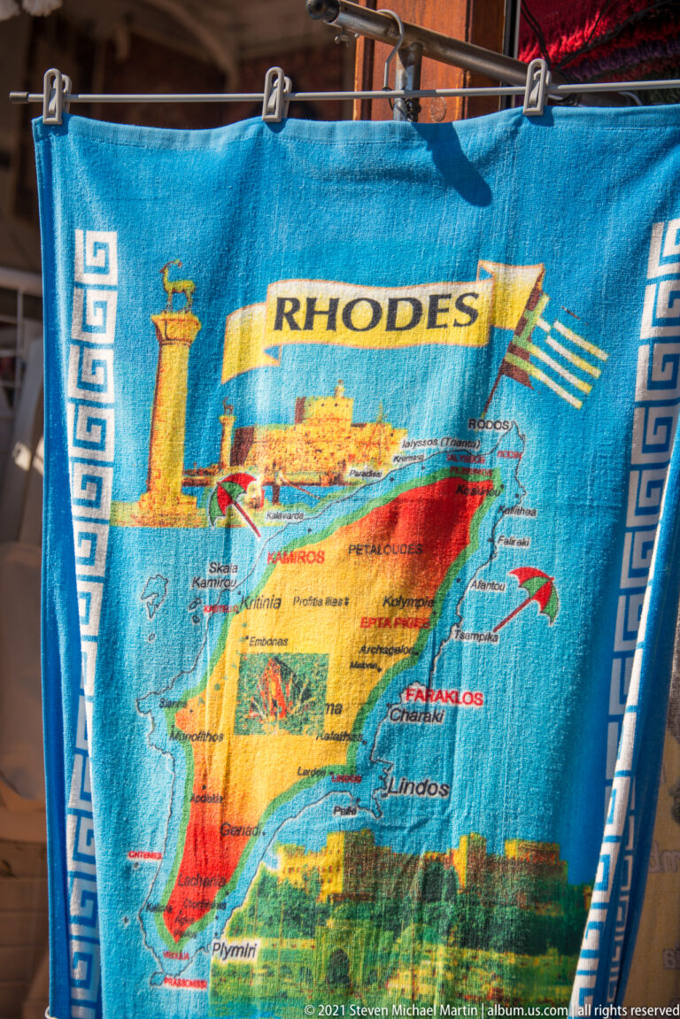 Blue souvenir textile printed with a map of Rhodes, place names, Greek-key borders, a column, and Greek flag.