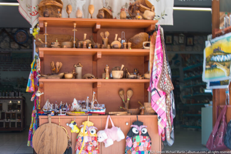 Shop shelves filled with wooden bowls and utensils, model sailboats, cutting boards, textiles, and colorful hanging souvenirs.