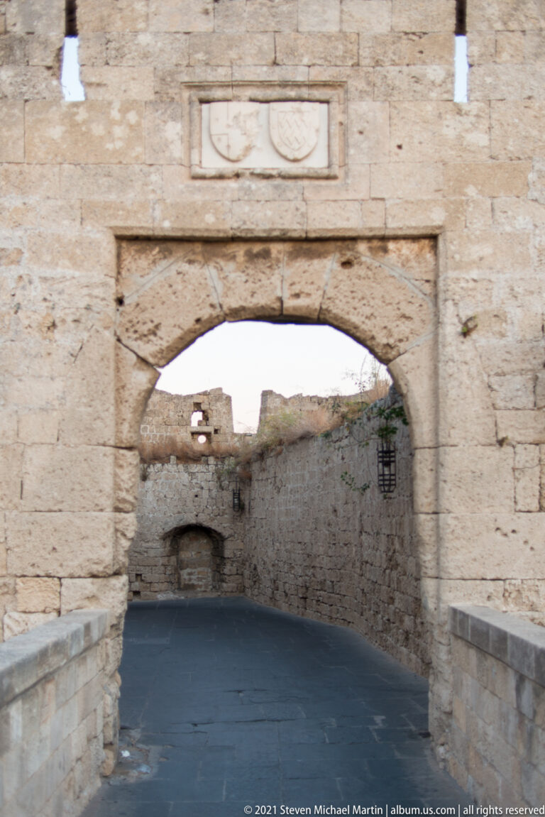 Broad stone arch spanning a paved passage between thick fortified walls in Rhodes Old Town.
