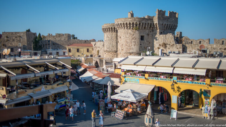 Busy commercial square with souvenir shops and pedestrians below a large crenellated round stone tower.