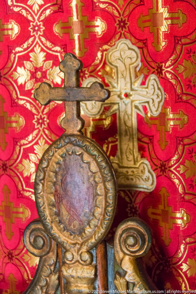 Ornate circular sacred medallion and metal cross displayed against richly patterned red church textile.