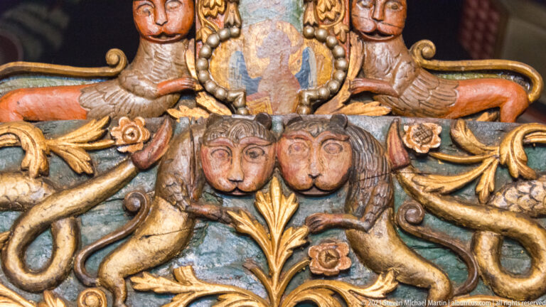 Carved iconostasis detail with two facing lion-like figures, gilded foliage, and a small sacred image above.