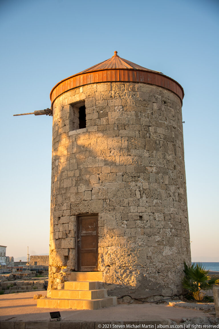 Cylindrical stone windmill with red-brown conical roof, wooden door, small opening, and projecting timber spar.