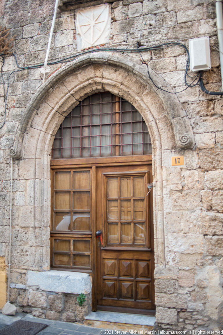 Large wooden doorway in a pointed stone arch with a pale carved relief above.