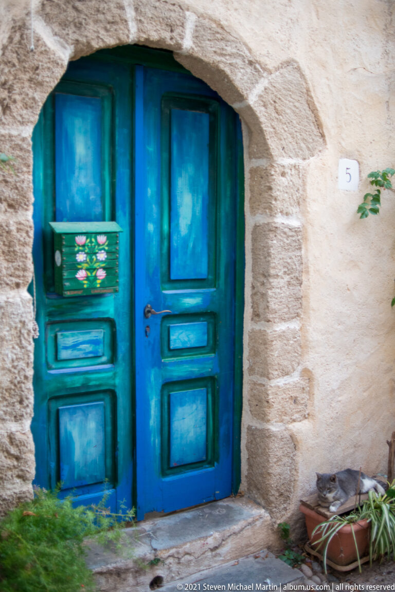 Weathered turquoise double doors set beneath a shallow stone arch with potted plants nearby.