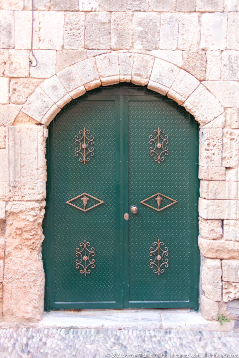 Green double metal gate with gold geometric motifs set in a low stone arch.