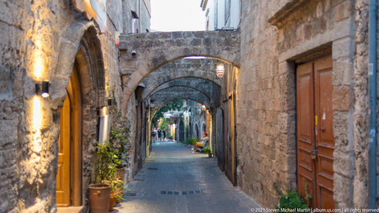Narrow stone pedestrian lane crossed by several overhead arches and lined with lit doorways.