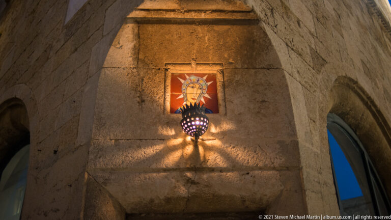 Religious icon mounted on rough stone above a perforated hanging lamp casting patterned light.