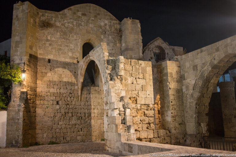 Roofless stone ruins with tall pointed arches and partial walls illuminated against the night sky.