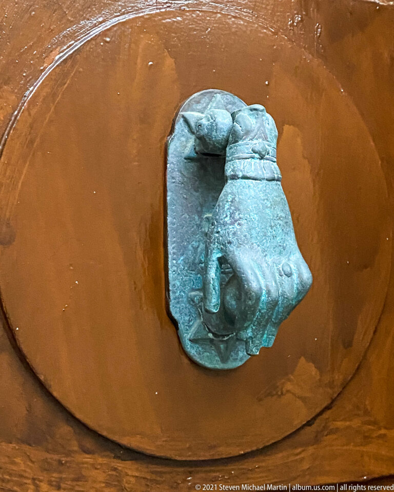 Green-patinated animal-head fountain spout pouring a thin stream of water against a terracotta-colored basin surface.