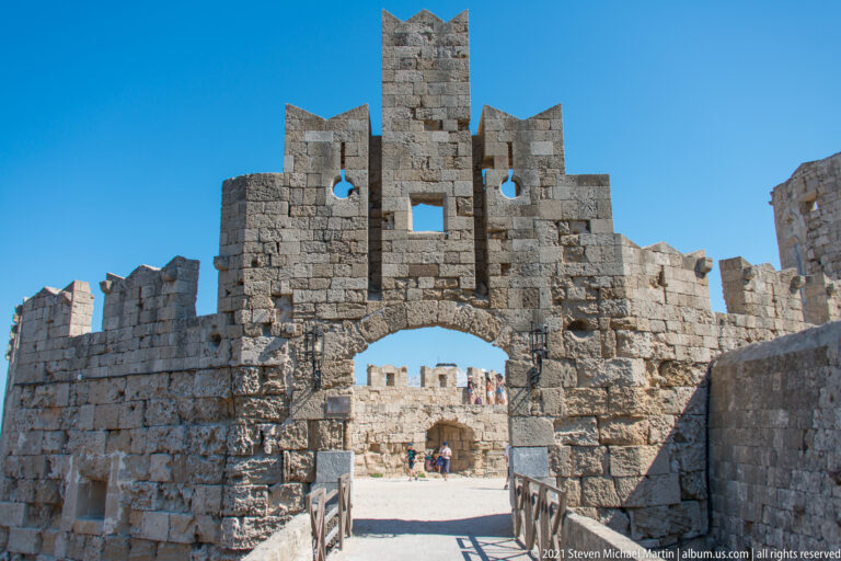 Weathered stone gate with a tall stepped parapet and a narrow walkway leading through successive arches.