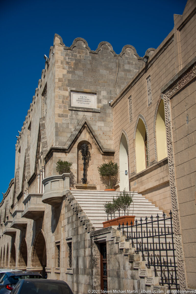 Exterior stair and balcony on a monumental stone façade with pointed openings and crenellated decoration.