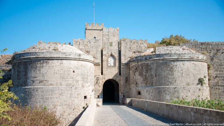 Stone bridge leading to an arched fortified gate between two massive rounded bastions.