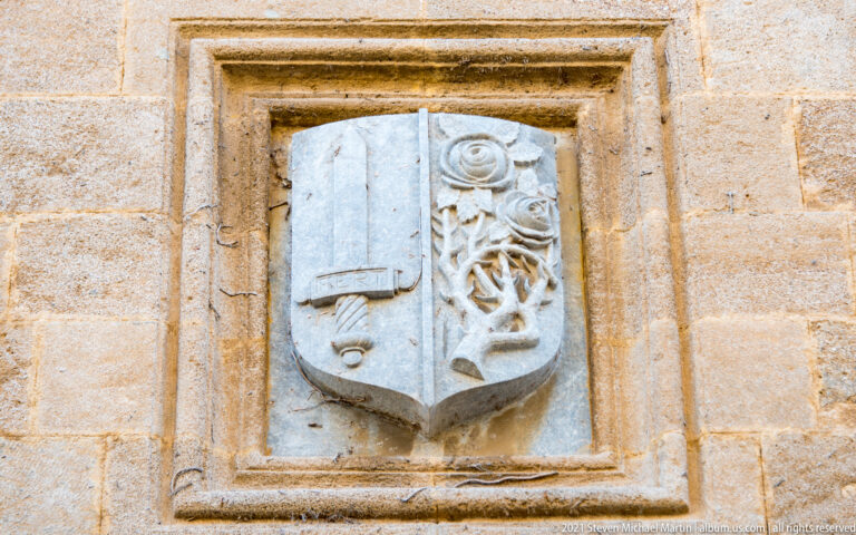 Divided stone heraldic shield with a simple geometric device on one side and ornate vegetal carving on the other.