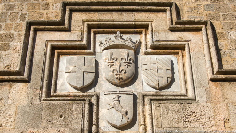 Cross-shaped heraldic panel with a crowned fleur-de-lis shield surrounded by four smaller coats of arms.