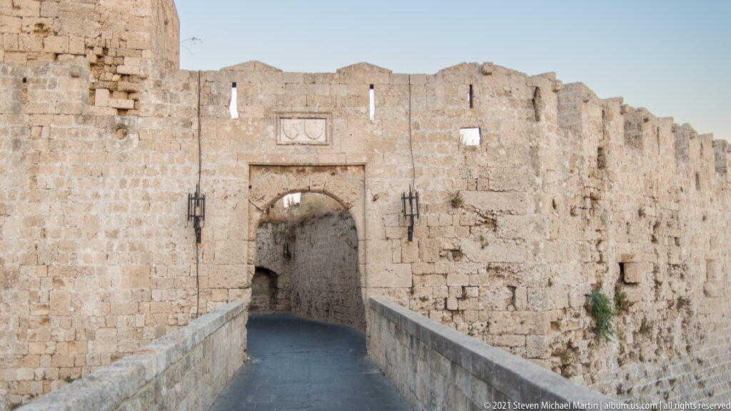 Stone arched gateway at the end of a narrow raised roadway through the fortified wall.