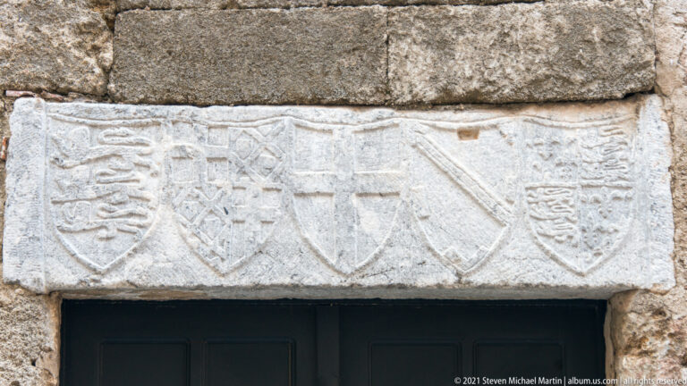 Stone lintel above a doorway carved with five weathered heraldic shields in a horizontal row.