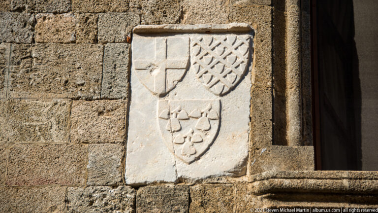 Three weathered stone shields showing a cross, diagonal lattice, and clustered rounded motifs beside a doorway.