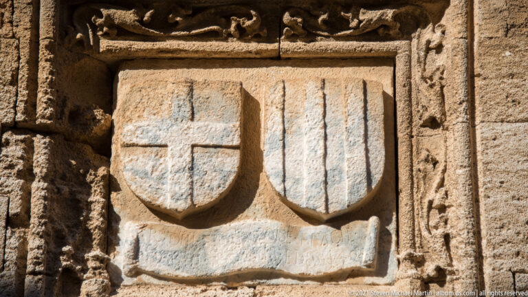Two carved stone shields side by side, one bearing a cross and the other vertical bars.