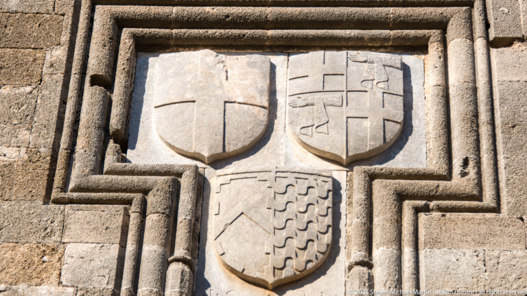Three carved heraldic shields within a stepped stone frame, including cross motifs and a divided lower shield.