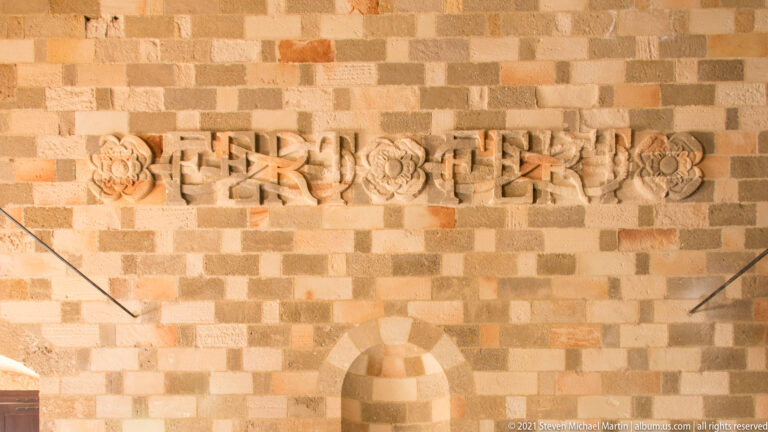 Row of carved stone ornamental fragments with rosettes and interlaced motifs mounted on a multicolored block wall.