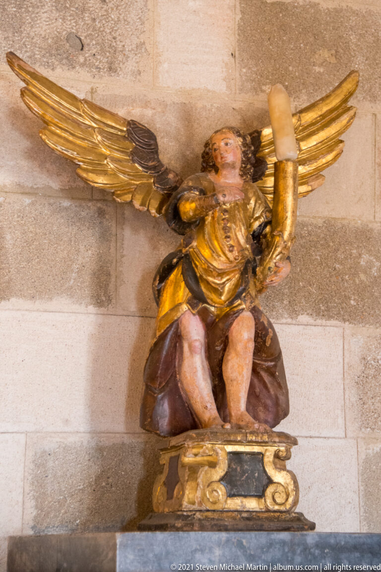 Kneeling painted angel with outspread gilded wings raising a large candle socket beside its head.