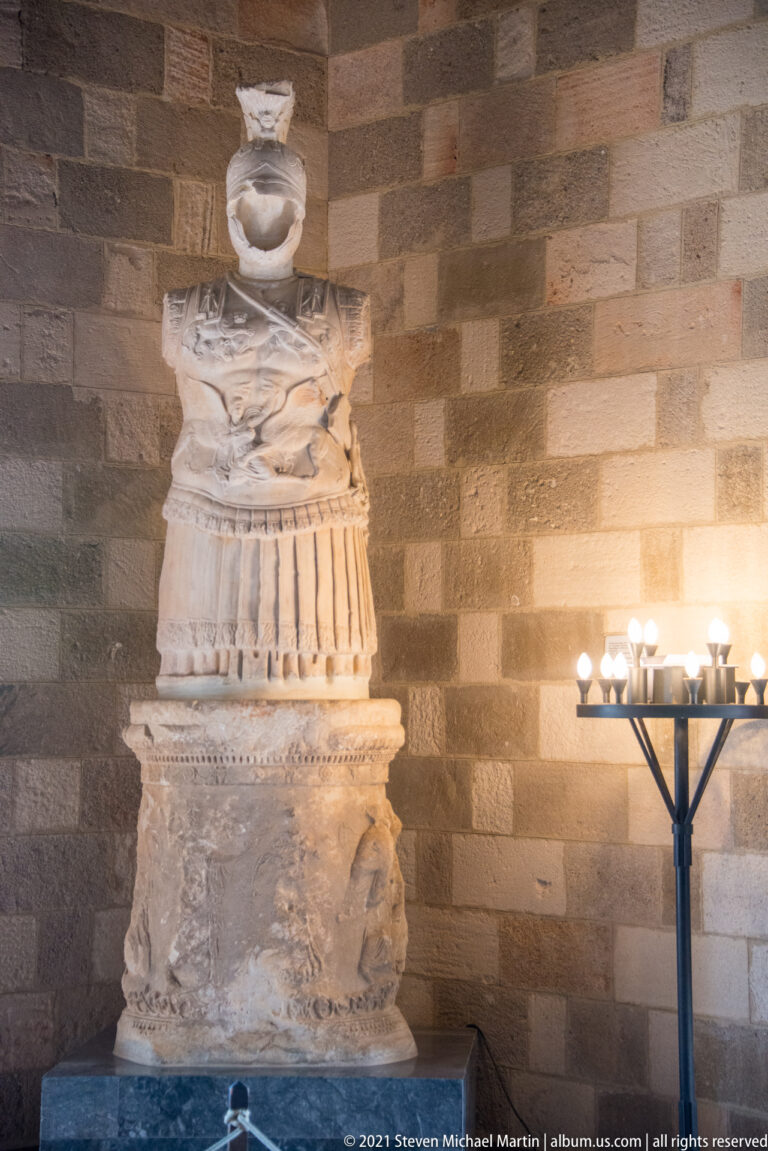 Tall carved stone pedestal assembled from relief-carved, fluted, and sculpted sections, with a shallow element at the top.
