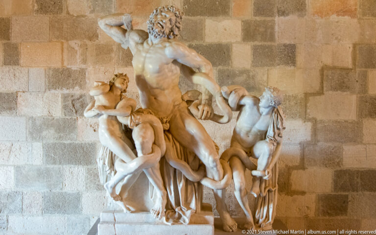 Marble sculptural group of a muscular bearded man and two youths twisting together in a dramatic struggle.