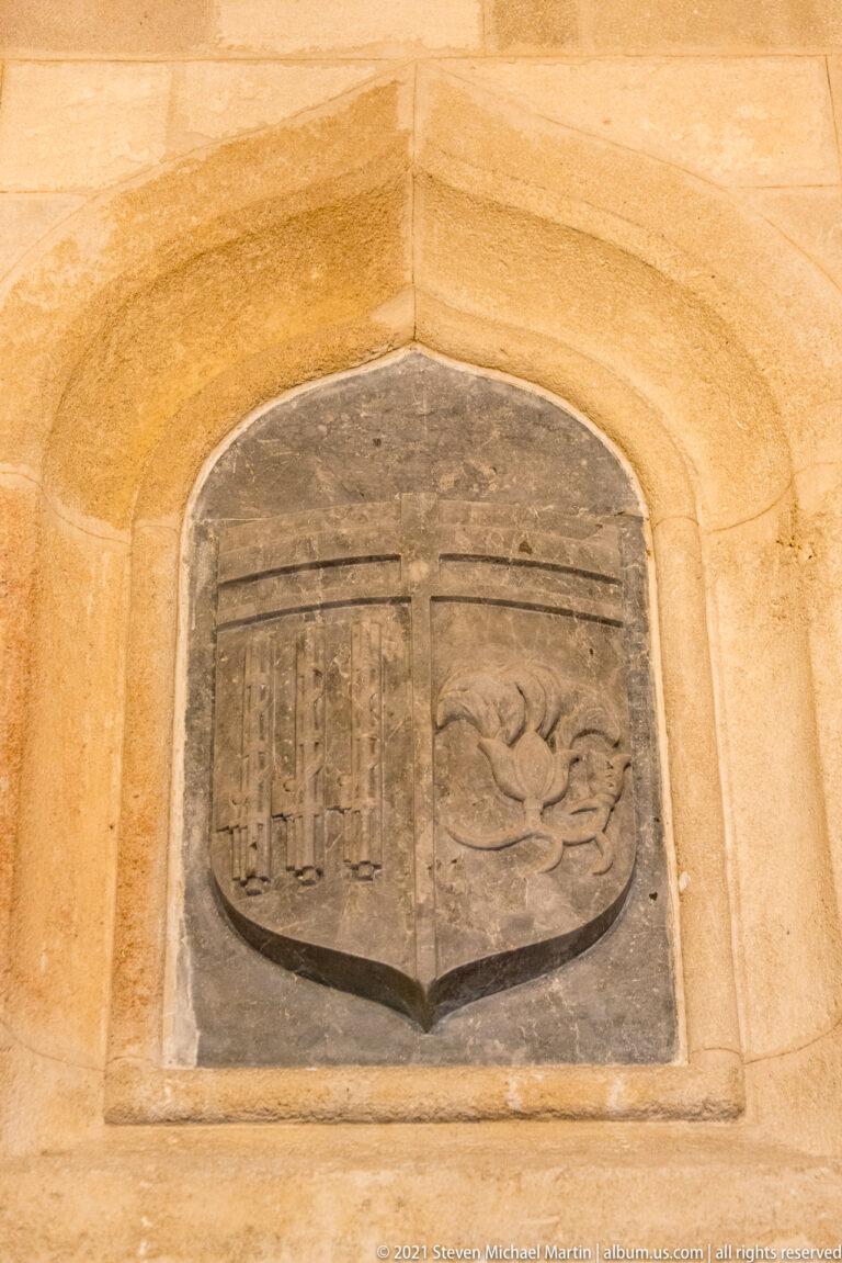 Shield-shaped carved stone relief in a pointed-arched niche, divided into two fields with different heraldic motifs.