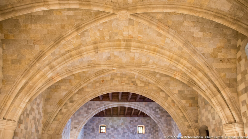 Concentric pointed stone arches rise toward a timber ceiling, with two small windows visible in the patterned masonry beyond.