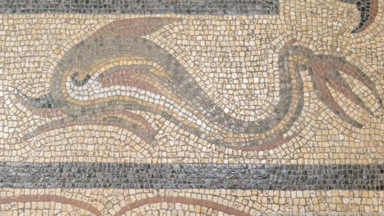 Close-up of pale mosaic pavement with a curving dark and red ribbon motif and a straight dark band below.