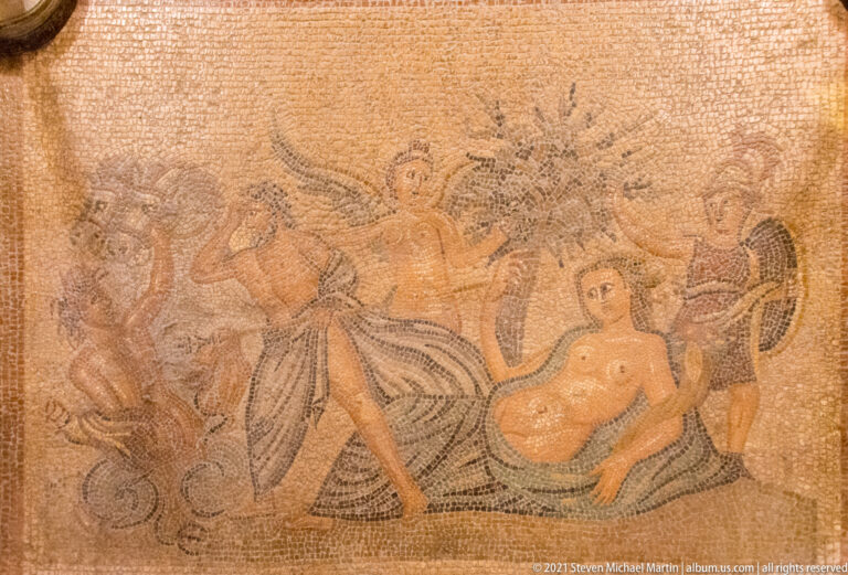 Ancient figurative mosaic with a central standing figure, reclining nude figure, and several surrounding figures or creatures.