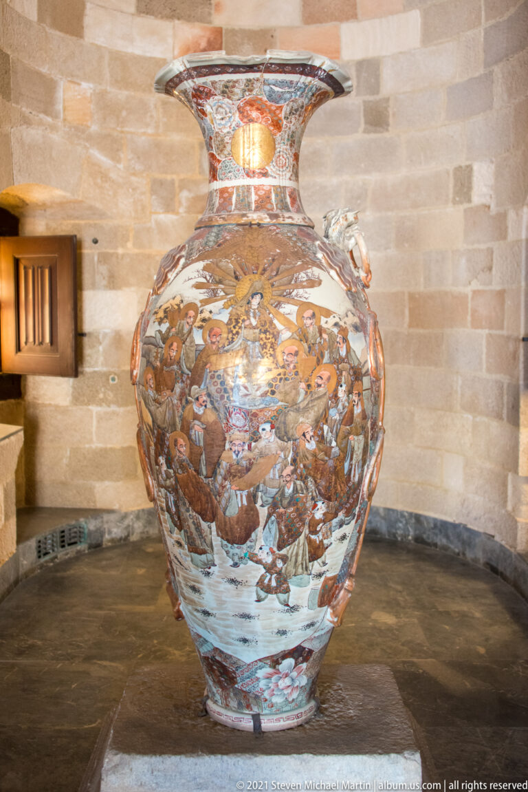 Large bulbous ceramic vase with flared neck and dense multicolored decoration of figures, animals, foliage, and patterned bands.