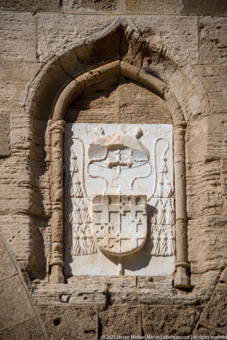 Weathered carved stone coat of arms mounted above a small arched opening in the palace masonry.