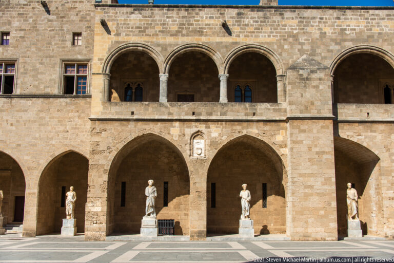 Two-story stone arcade in the courtyard with four statues standing beneath the lower arches.