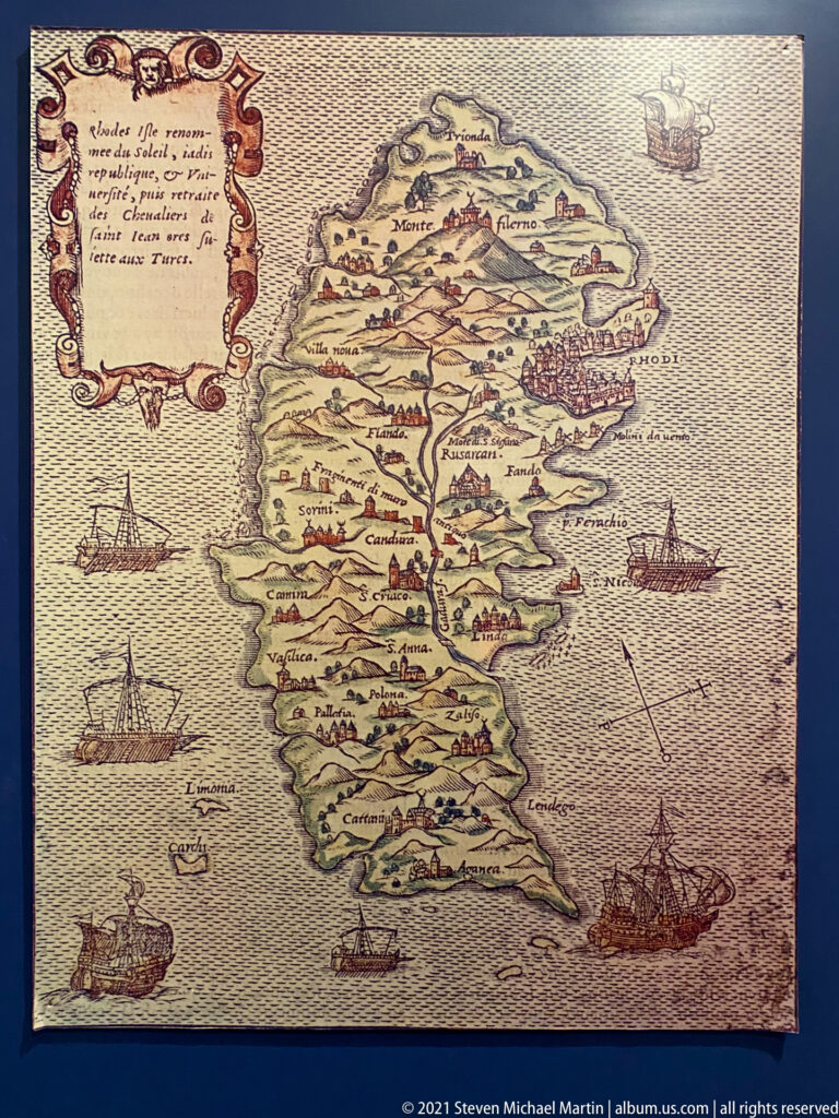 Historic printed map of Rhodes showing the island, labeled settlements and mountains, and sailing ships in the surrounding sea.