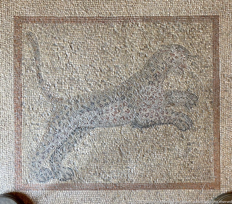 Faded rectangular mosaic panel with the worn outline of a large animal-like figure against a pale tessellated field.