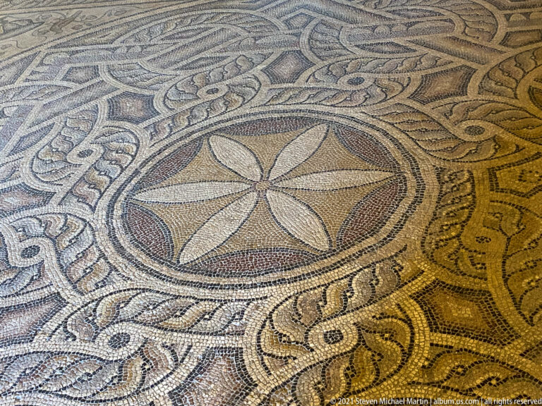 Ancient mosaic floor with a four-petaled rosette in a circular medallion surrounded by broad interlaced ornament.