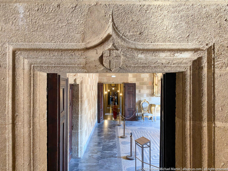 Carved stone doorway with a small shield-like motif in the lintel and a sequence of interior rooms visible beyond.