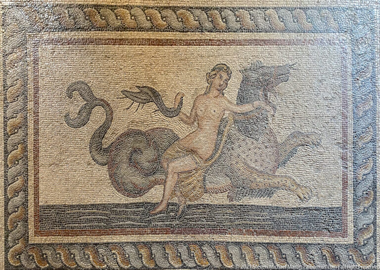 Ancient mosaic panel with a nude or lightly draped figure riding a large curling sea creature within a braided border.