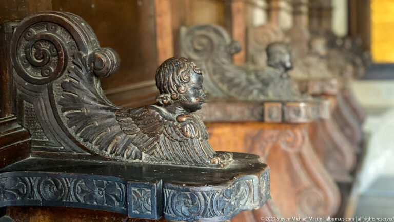 Close view of a dark carved wooden furniture terminal with scrollwork and a small sculpted figure.