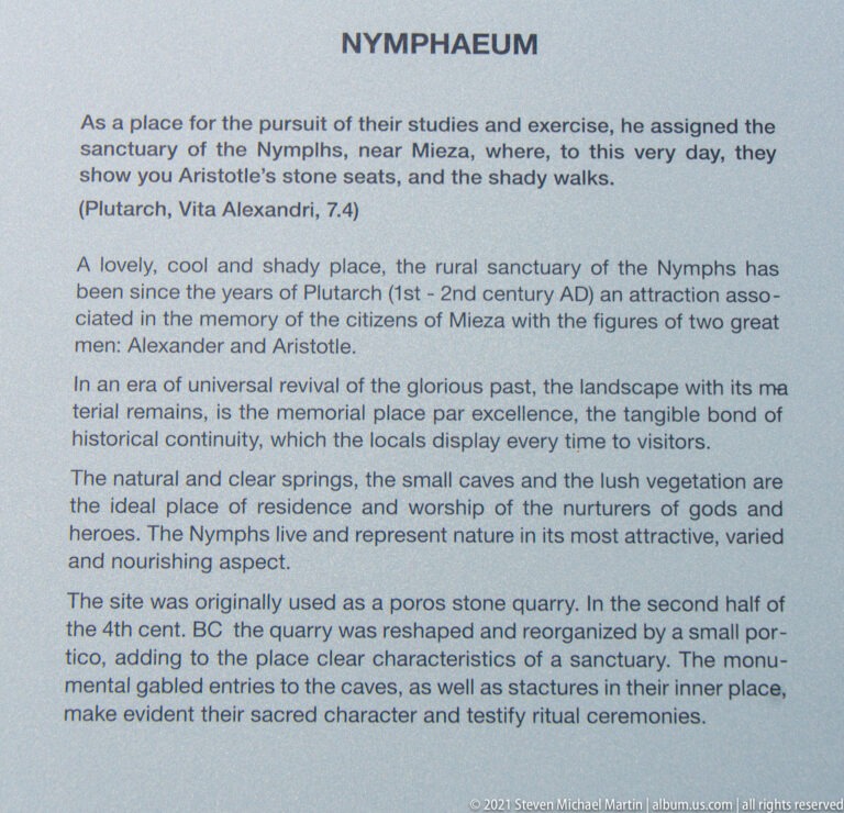Close view of an English interpretive panel headed “NYMPHAEUM,” with paragraphs about Mieza, Aristotle, Alexander, springs, and caves.