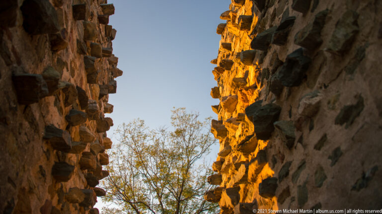 Narrow gap between rough historic masonry walls, with sunlight catching the right edge.