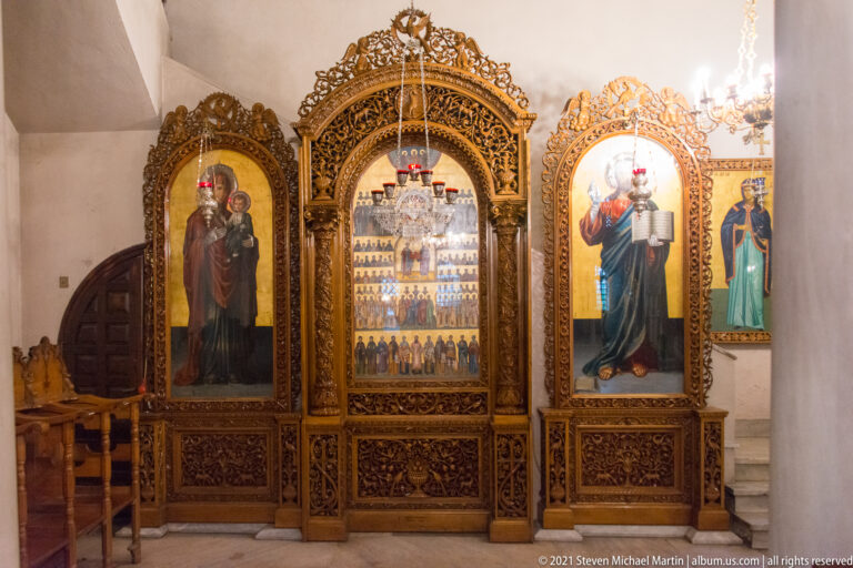 Carved wooden icon screen with three painted icons and hanging lamps inside an Orthodox church.